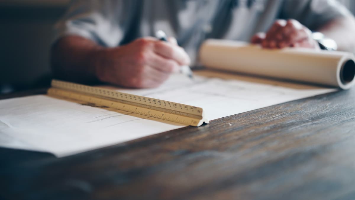 Hands drafting a plan with a pencil and scale ruler